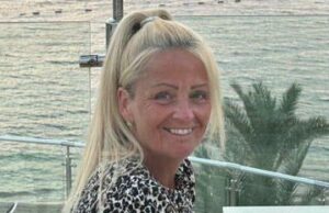 Presidente designado para depoimento à direita na fatalidade de Anita Rose Anita Rose está vestindo um topo de estampa de animais e sentou -se em frente a uma grade à beira do mar. Seu cabelo loiro está em um rabo de cavalo alto e ela está olhando diretamente para a câmera e sorrindo. No fundo é uma palmeira e o mar.