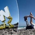 Um homem de costas em uma toalha de praia que apoia uma mulher em uma pose acrobática nos pés.