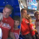 Uma mulher em um moletom de Phillies argumenta com um grupo de pessoas em um jogo de beisebol.