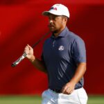 Golfer Xander Schauffele andando com um clube de golfe por cima do ombro.