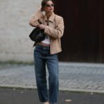 PARIS, FRANÇA - 20 DE MAIO: Ellie Delphine usa brincos dourados, um colar da Missoma, uma blusa / camisa bege oversized sem ombros da The Frankie Shop, calças jeans / jeans azuis de perna larga da H&M, uma bolsa de couro preta da Neous, sandálias T / sapatos de salto alto da Neous, durante uma sessão de fotos de moda de estilo de rua, em 20 de maio de 2024 em Paris, França. (Foto de Edward Berthelot/Getty Images)