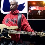 Sam Rivers do Limp Bizkit se apresentando ao vivo, segurando um baixo enquanto usava um moletom vermelho.