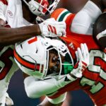 Malachi Toney #10 of the Miami Hurricanes battles defensive back Tayon Holloway #25 of the Louisville Cardinals