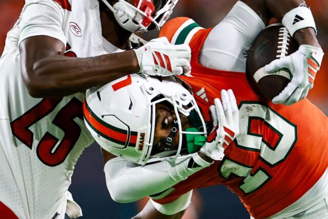 Malachi Toney #10 of the Miami Hurricanes battles defensive back Tayon Holloway #25 of the Louisville Cardinals