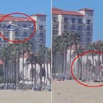 Nuvem de poeira surge de um acidente de helicóptero em Huntington Beach, Califórnia, com banhistas e edifícios ao fundo.
