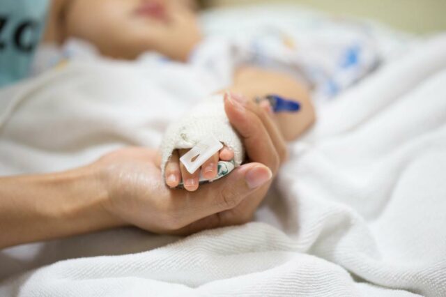 A mão de uma mãe segurando a mão de um bebê, que possui um tubo IV médico anexado.