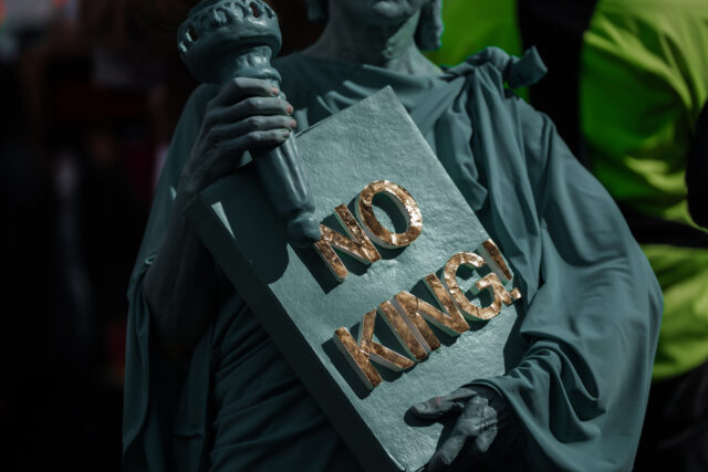 Um manifestante carrega uma placa enquanto se manifesta no corredor da rua 14 com U antes de marchar para o National Mall durante um protesto No Kings em Washington, sábado, 18 de outubro de 2025. (AP Photo/Jose Luis Magana)