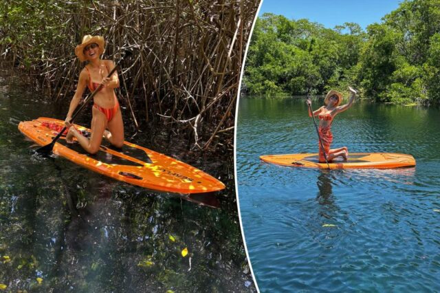 Brie Larson se ajoelhando em um paddle de laranja em um corpo de água com árvores verdes exuberantes ao fundo.