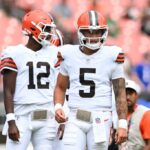 O jogador de Cleveland Browns usando Jersey Número 5 com tatuagens de braço visível fica no campo ao lado de outro jogador.