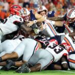 Jogadores do Georgia Bulldogs enfrentando um jogador do Auburn Tigers que está mergulhando para a end zone.