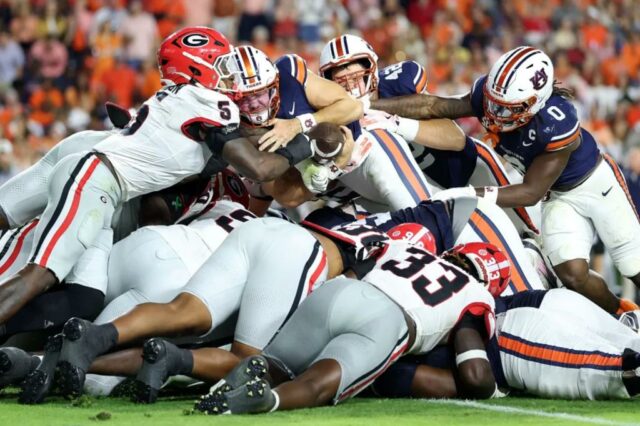 Jogadores do Georgia Bulldogs enfrentando um jogador do Auburn Tigers que está mergulhando para a end zone.