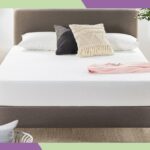 Colchão branco sobre cama marrom com cabeceira texturizada, almofadas decorativas e manta rosa na cama.