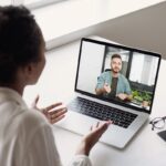 Woman on a video call with a man on a laptop screen in an office setting.