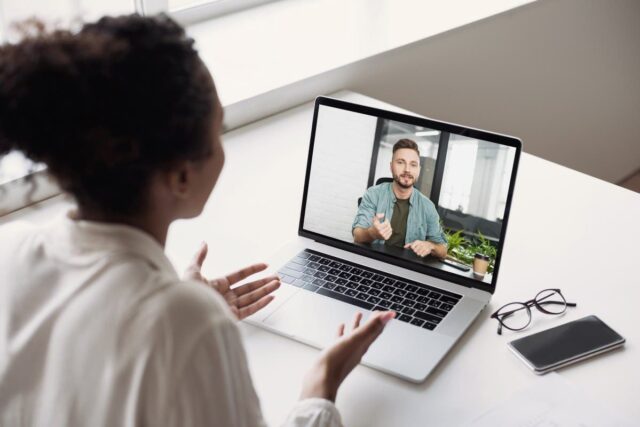Woman on a video call with a man on a laptop screen in an office setting.