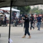 Um membro das forças de segurança interna leais ao grupo palestiniano Hamas organiza o tráfico enquanto pessoas deslocadas que regressam à Cidade de Gaza conduzem com os seus pertences pelo campo de refugiados de Nuseirat, no centro da Faixa de Gaza, em 12 de outubro de 2025.