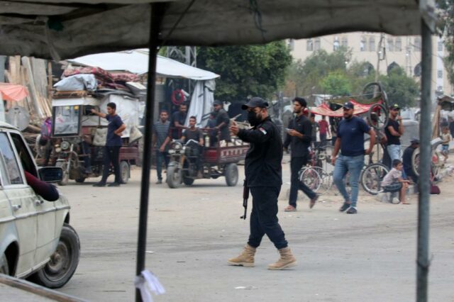 Um membro das forças de segurança interna leais ao grupo palestiniano Hamas organiza o tráfico enquanto pessoas deslocadas que regressam à Cidade de Gaza conduzem com os seus pertences pelo campo de refugiados de Nuseirat, no centro da Faixa de Gaza, em 12 de outubro de 2025. 