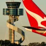 Um avião Qantas Airbus A330-202, matrícula VH-EBM, passando pela torre de controle de tráfego aéreo enquanto taxia no Aeroporto Sydney Kingsford-Smith em preparação para a partida como voo QF43 para Denpasar.