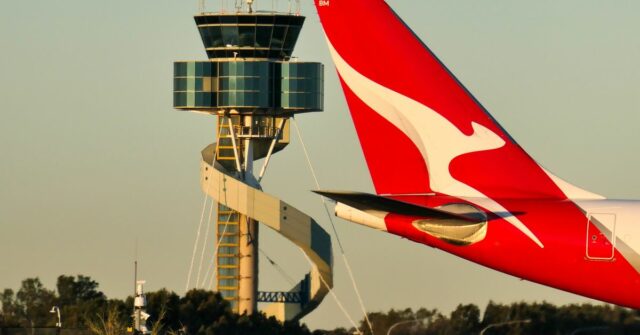 Um avião Qantas Airbus A330-202, matrícula VH-EBM, passando pela torre de controle de tráfego aéreo enquanto taxia no Aeroporto Sydney Kingsford-Smith em preparação para a partida como voo QF43 para Denpasar. 