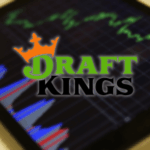DraftKings adquire Railbird para expandir em mercados de previsões. Logotipo DraftKings com uma coroa laranja acima do texto verde e preto sobre um fundo desfocado mostrando um mercado de ações ou gráfico financeiro em uma tela.