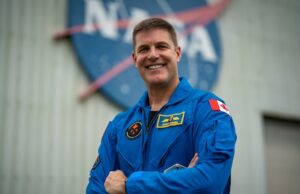 Em 4 meses, o canadense Jeremy Hansen certamente será lançado para a lua- onde ele também será um assunto de teste humano Quatro astronautas em macacões azuis estão sentados em um palco e viram para olhar para um vídeo de si mesmos em trajes espaciais de laranja.