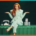 Uma mulher sorridente alimenta um bebê feliz com uma mamadeira, com um recipiente de Fórmula Infantil Orgânica Bobbie sobre a mesa.