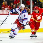 O pivô do Rangers, JT Miller (8), e o pivô do Calgary Flames, Mikael Backlund (11), lutam pelo disco durante o terceiro período no Scotiabank Saddledome.