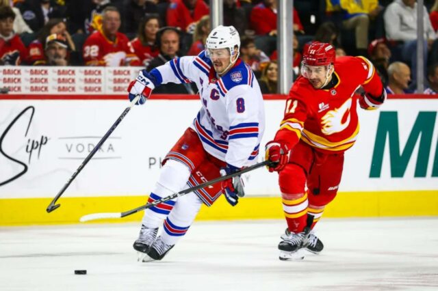 O pivô do Rangers, JT Miller (8), e o pivô do Calgary Flames, Mikael Backlund (11), lutam pelo disco durante o terceiro período no Scotiabank Saddledome. 