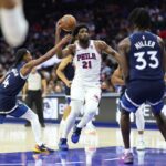 O pivô do Philadelphia 76ers, Joel Embiid (21), dirige entre o guarda do Minnesota Timberwolves, Rob Dillingham (4) e o atacante Leonard Miller (33).