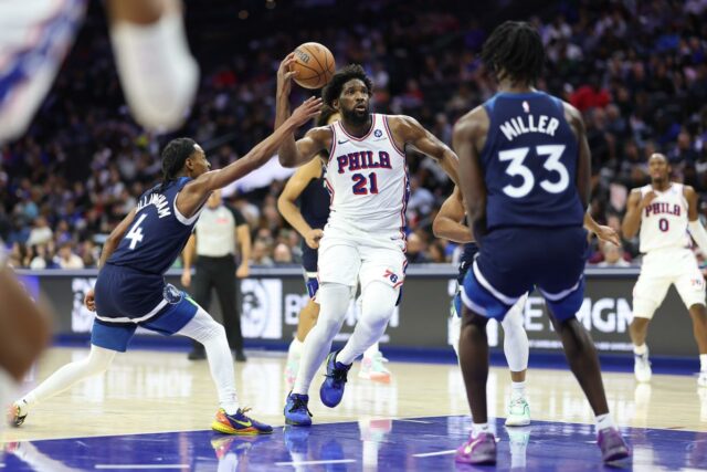 O pivô do Philadelphia 76ers, Joel Embiid (21), dirige entre o guarda do Minnesota Timberwolves, Rob Dillingham (4) e o atacante Leonard Miller (33).