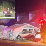 Um carro dourado bateu em uma tenda branca de festa à noite, com luzes vermelhas de emergência piscando.