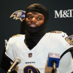 O jogador de futebol Lamar Jackson vestindo uma balaclava preta e uma camisa branca dos Ravens.