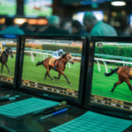 Uma fotografia em close de várias telas de corridas de cavalos dentro de uma casa de apostas mal iluminada, exibindo imagens de corridas ao vivo com puros-sangues galopando contornando uma pista. Ataque fiscal sobre apostas pode ameaçar 40.000 empregos no Reino Unido, alerta análise