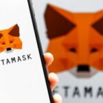 MetaMask está fazendo parceria com a Polymarket. Logotipo da raposa MetaMask visto no smartphone e no fundo