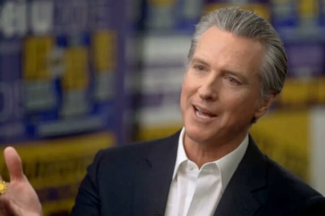 O governador da Califórnia, Gavin Newsom, finalmente confirma suas ambições Governador da Califórnia, Gavin Newsom, vestindo terno, falando durante uma entrevista com um fundo desfocado do SEIU 2020.
