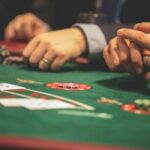 Tribos da Califórnia foram impedidas de processar salas de jogos por direitos exclusivos do estado. Close de pessoas jogando pôquer em uma mesa de cassino, com cartas de baralho, fichas e mãos visíveis na superfície de feltro verde.