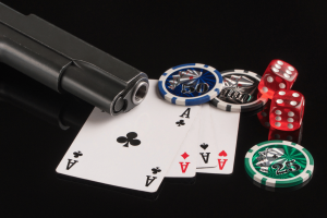 O que você precisa saber sobre os mafiosos intrometidos na O que você precisa saber sobre os mafiosos acusados de escândalo de jogos de pôquer fraudulentos. Fichas de pôquer, cartas e uma arma em um fundo preto. O conceito de jogos de azar e entretenimento.