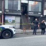 A polícia investigando uma cena de assassinato na 7 Eldridge Street, com fita amarela do outro lado das escadas externas do prédio e policiais em pé na rua.