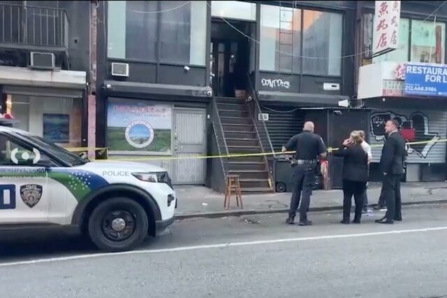A polícia investigando uma cena de assassinato na 7 Eldridge Street, com fita amarela do outro lado das escadas externas do prédio e policiais em pé na rua.