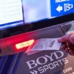 Close de uma mão pegando um pedaço de papel semelhante a um recibo de um. Máquina Boyd Sports. Boyd Gaming atinge receita de US$ 1 bilhão no terceiro trimestre, afirma relatório