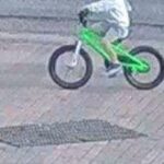 Uma imagem granulada de CCTV de um menino andando de bicicleta em uma bicicleta BMX verde brilhante. Sua cabeça está fora do quadro.