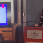 Mulher de óculos e blusa preta fica atrás de um pódio enquanto faz um discurso, com uma TV à sua esquerda. Nação Seneca gera impacto de quase US$ 2 bilhões na economia do oeste de Nova York