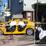 Um táxi amarelo bateu em um prédio e em um poste na esquina da W 42 St com a 12th Avenue, com fita policial bloqueando a cena e dois policiais parados nas proximidades.