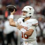 Arch Manning nº 16 do Texas Longhorns sentado no chão, segurando a perna durante um jogo de futebol.