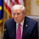 Donald Trump vestindo terno escuro e gravata rosa, com distintivo de lapela com a bandeira dos EUA.