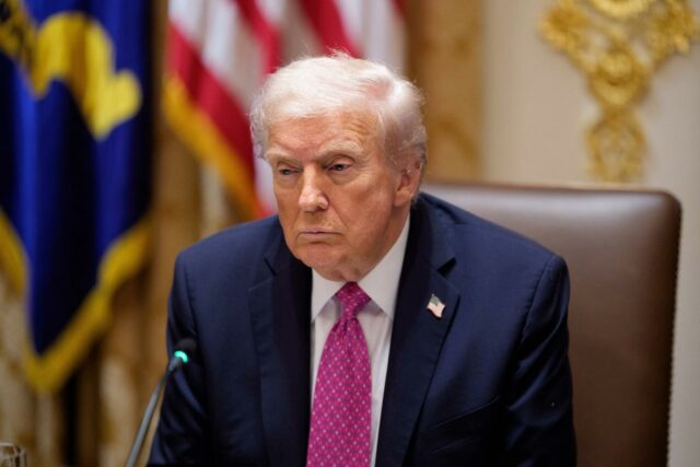 Trump anuncia aumento de tarifas de 10% sobre o Canadá Donald Trump vestindo terno escuro e gravata rosa, com distintivo de lapela com a bandeira dos EUA.