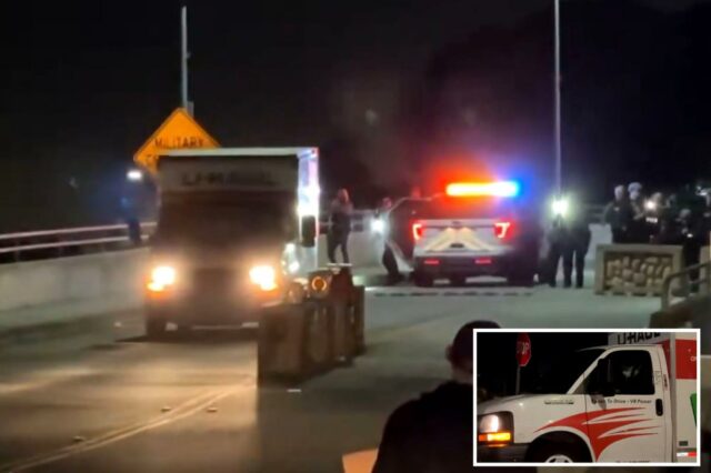 Um caminhão U-Haul dirige-se em direção a um veículo policial iluminado e policiais à noite.