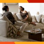 Sala de jantar com mesa redonda de madeira, quatro cadeiras estofadas em cinza claro e estantes decorativas.