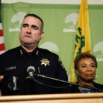 O chefe de polícia de Oakland, Floyd Mitchell, à esquerda, observa enquanto a prefeita de Oakland, Barbara Lee, faz o discurso do estado de Oakland na Prefeitura de Oakland em Oakland, Califórnia, na terça-feira, 7 de outubro de 2025. (Ray Chavez/Bay Area News Group)