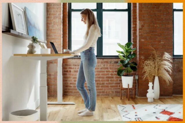 Cadeira de escritório cinza claro com braços e base cromada com rodas ao lado de uma mesa branca.