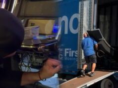 A repressão ao jogo na Flórida continua com outras 134 máquinas caça-níqueis apreendidas A repressão ao jogo na Flórida continua com a apreensão de outras 134 máquinas caça-níqueis. Duas cenas combinadas: à esquerda, uma pessoa com capuz parece inspecionar ou manipular uma máquina caça-níqueis em um ambiente escuro; à direita, um trabalhador de camisa azul carrega uma grande máquina de jogos em um caminhão em movimento usando uma rampa.